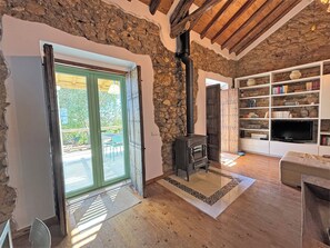 A rustic interior with a stone wall, wooden beams, a fireplace, and a bookshelf.
