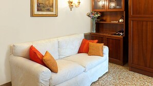 A living room with a white sofa, two orange cushions, a wooden cabinet with glass doors, a framed picture on the wall, and a vase with flowers. - 'Palazzo Rossi' Apartment 3B in the old town with balcony, free parking and WiFi (Treviso)