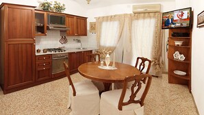 A compact kitchen with wooden cabinets, a stove, and a dining table with chairs.