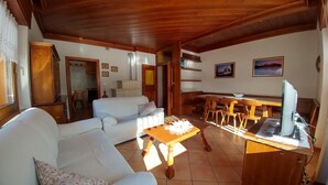 A cozy living room with a white sofa, a wooden coffee table, and a dining area with wooden chairs and a table. - APARTMENT IN THE WHITE MAGIC OF THE DOLOMITES (Laggio di Cadore)