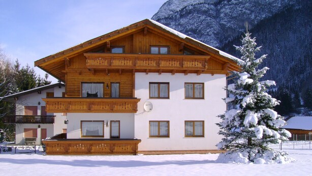A multi-story wooden chalet with balconies and large windows, surrounded by snow-covered mountains. - APARTMENT IN THE WHITE MAGIC OF THE DOLOMITES (Laggio di Cadore)