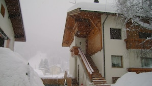 A snow-covered building with a staircase leading to a wooden door. - APARTMENT IN THE WHITE MAGIC OF THE DOLOMITES (Laggio di Cadore)