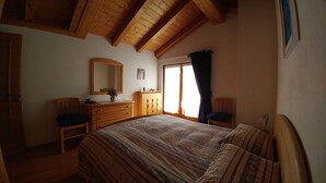 A bedroom with a wooden ceiling, a bed with striped bedding, a dresser, a mirror, and a window with curtains. - APARTMENT IN THE WHITE MAGIC OF THE DOLOMITES (Laggio di Cadore)
