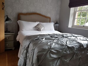 Classic bedroom with a silver quilted duvet, decorative pillow, and wooden headboard.