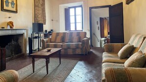 A living room with a sofa, a table, a television, a fireplace, and a chandelier. - Spacious house between Siena e Firenze with private swimming pool, A/C and Wi-Fi (Radicondoli)