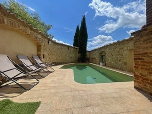 A courtyard with a swimming pool, lounge chairs, and stone walls.