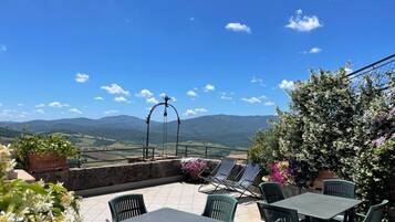 A terrace with tables and chairs, a hanging light fixture, and a view of the countryside.