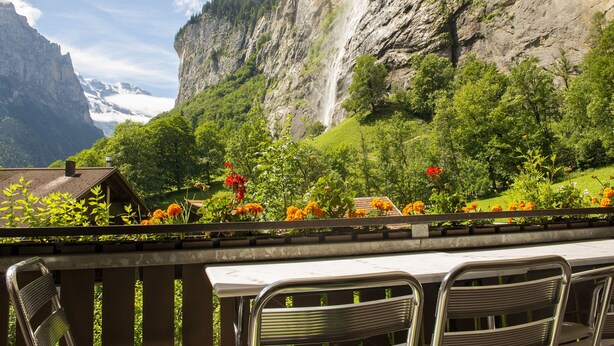 A terrace with metal chairs and a table, overlooking a waterfall and lush greenery. - 2 BALCONIES,1 TERRACE,VIEWS OF  WATERFALL, MOUNTAINS, RIVER,WENGEN,TRAINS, (Lauterbrunnen)