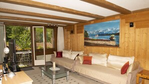 A cozy living room with a sofa, a glass coffee table, and a painting of a lake and mountains on the wall. - 2 BALCONIES,1 TERRACE,VIEWS OF  WATERFALL, MOUNTAINS, RIVER,WENGEN,TRAINS, (Lauterbrunnen)
