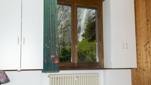 A bedroom with a bed, a window with a view of a waterfall, a radiator, and wooden walls. - 2 BALCONIES,1 TERRACE,VIEWS OF  WATERFALL, MOUNTAINS, RIVER,WENGEN,TRAINS, (Lauterbrunnen)