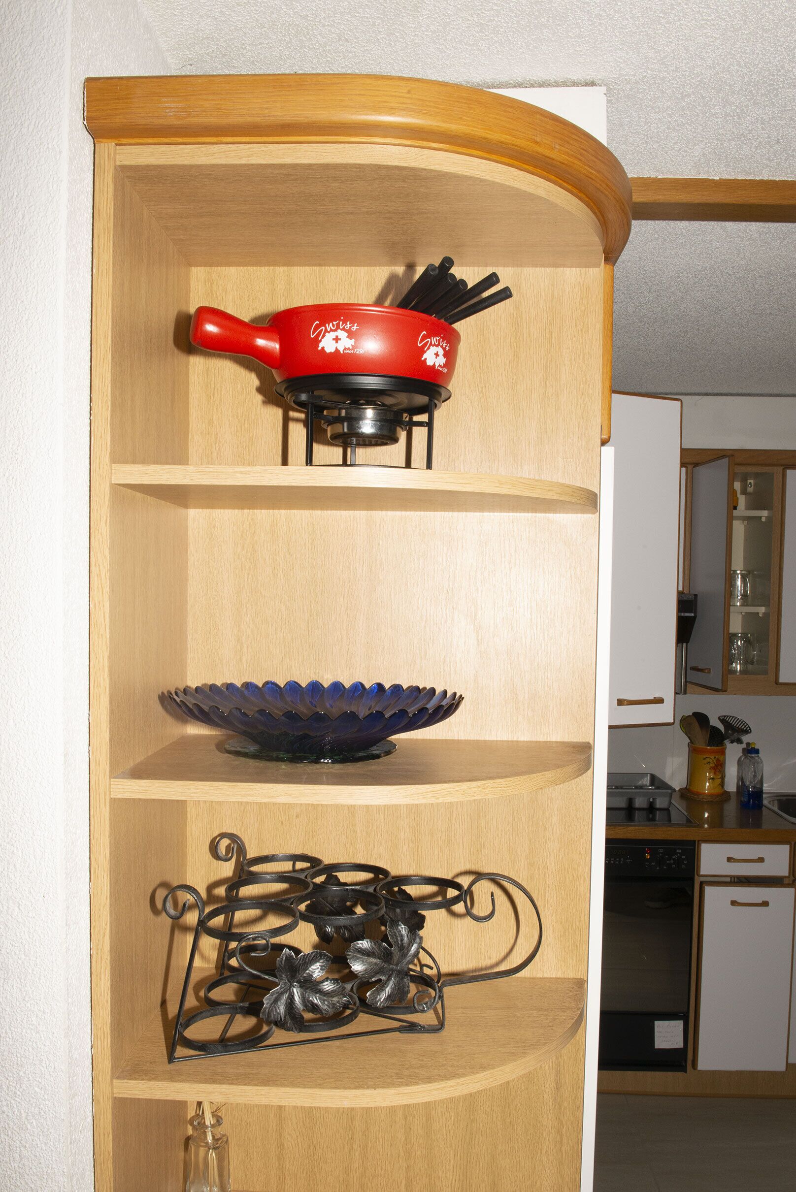 Una cocina con estantes de madera, una olla roja, un tazón azul y una escultura de metal.