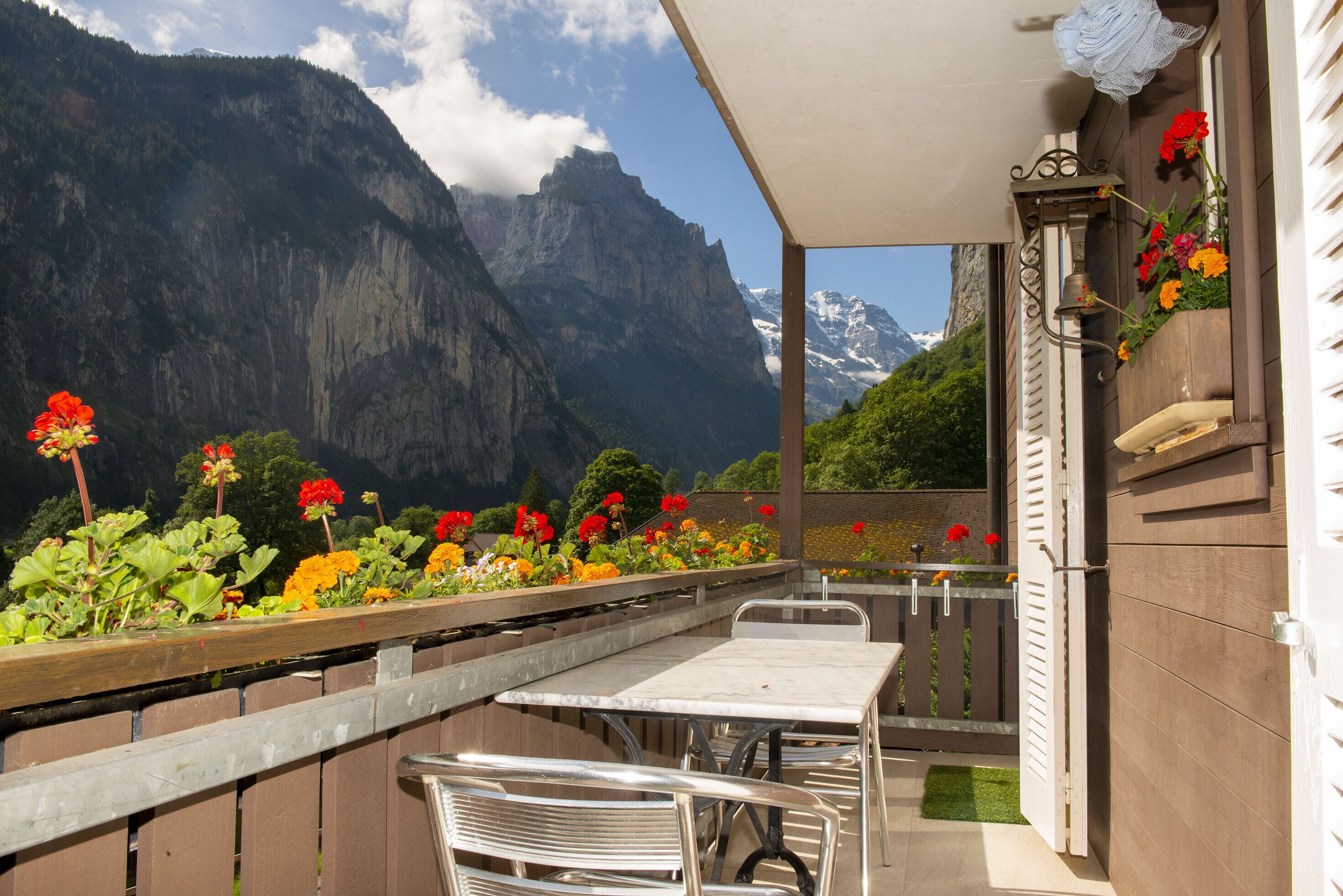 En balkon med et bord og stole, udsigt til et bjerglandskab med blomster og et træhegn.