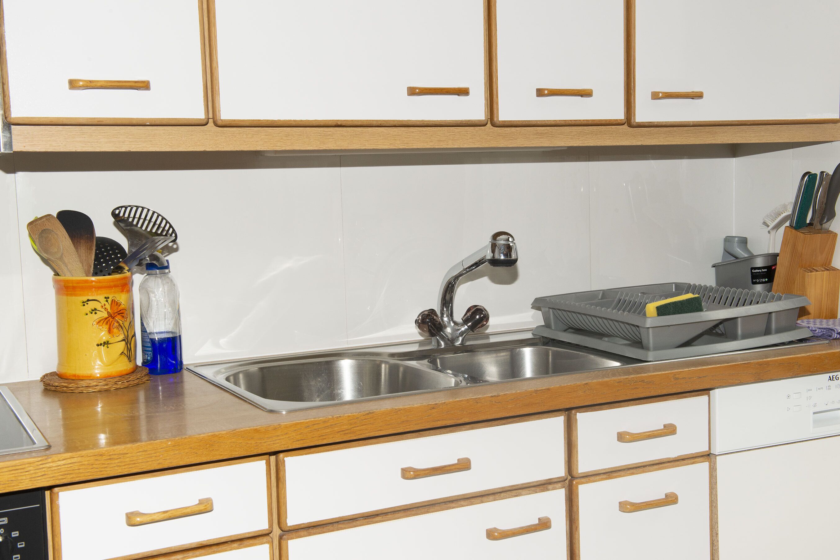 Una cocina con armarios de madera, un lavamanos de acero inoxidable y diversos utensilios.