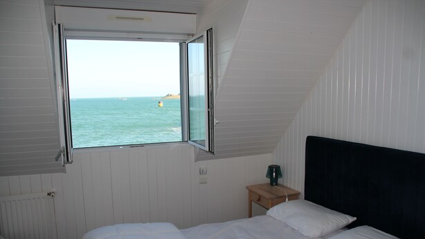 A bedroom with a large window, a bed, a bedside table, and a chair. - BZ sea view and close to town center (Roscoff)
