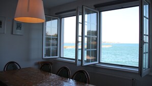 A dining area with a table and chairs, large windows with ocean views, and a hanging light fixture. - BZ sea view and close to town center (Roscoff)