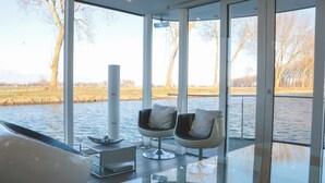 Une chambre moderne avec de grandes fenêtres donnant sur un plan d’eau, deux fauteuils et une petite table agrémentée d’un objet décoratif.