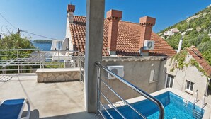 A rooftop swimming pool with a view of the sea, a stone wall, and a building with a tiled roof. - Gorgeous villa with unforgettable view and swimming pool (Dubrovnik)