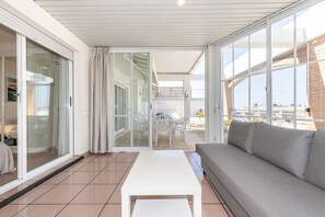A modern living room with a sofa, a white table, and a glass door leading to an outdoor patio. - AirCon Penthouse Sea Views · Parking Pool · CENTER II 113 (Salou)