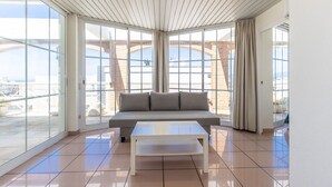Een modern interieur met een bank, een salontafel en grote ramen met uitzicht op de lucht en een bakstenen gebouw buiten.