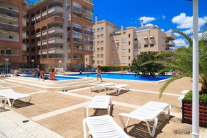 A swimming pool area with lounge chairs, a pool, and multi-story buildings in the background.