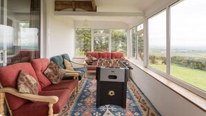 A cozy room with a foosball table, comfortable seating, and large windows offering a view of the countryside. - Large Holiday Cottage for families, groups near Bude in Cornwall (Bude)