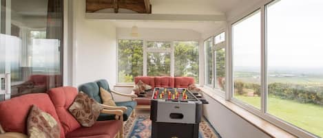 A cozy room with a foosball table, comfortable seating, and large windows offering a view of the countryside.
