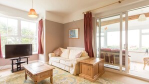 A living room with a sofa, a TV, a wooden coffee table, and a patterned rug. - Large Holiday Cottage for families, groups near Bude in Cornwall (Bude)