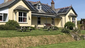 A two-story house with a covered patio area, solar panels on the roof, and a grassy lawn. - Large Holiday Cottage for families, groups near Bude in Cornwall (Bude)
