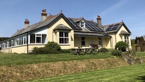 A large, single-story house with a sloped roof, multiple chimneys, and a small porch with benches. - Large Holiday Cottage for families, groups near Bude in Cornwall (Bude)