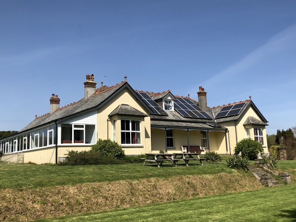 A large, single-story house with a sloped roof, multiple chimneys, and a small porch with benches. - Large Holiday Cottage for families, groups near Bude in Cornwall (Bude)