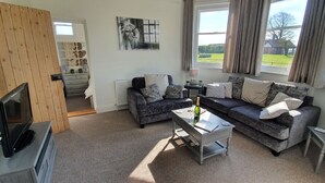 A living room with a sofa set, a coffee table, a TV, and a view of the outdoors. - Hinton Lodge - Quaint Victorian four star cottage in a quiet rural location. (Trowbridge)