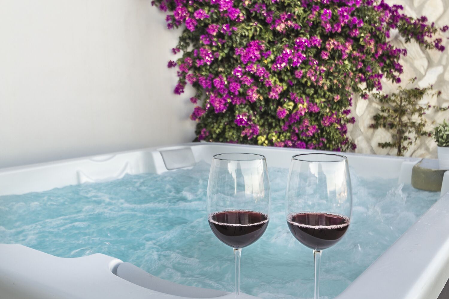 A hot tub with two glasses of red wine.