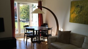 A living room with a sofa, coffee table, and dining table with chairs. There is a painting on the wall and a ceiling light fixture. - Beautiful Kingston apartment (Kingston upon Thames)