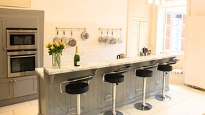 Una cocina con encimera de mármol, cuatro taburetes de bar, una botella de vino y un jarrón con flores.