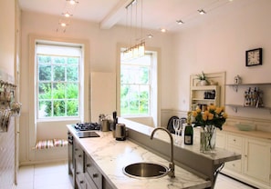 A modern kitchen with a marble countertop, stainless steel sink, and large windows.