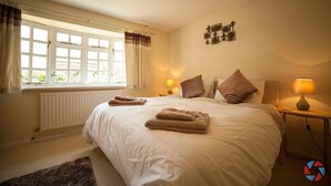 A bedroom with a large bed, two bedside lamps, a window with curtains, a radiator, and a small rug.