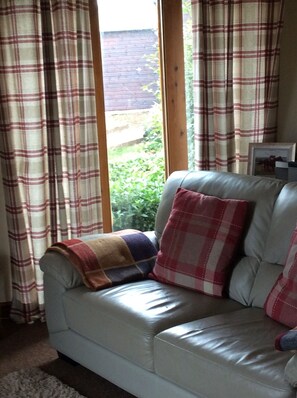 A white leather sofa with plaid cushions, a plaid blanket, and a framed picture on a wooden window sill. - Availability Sept 3rd -7th 4nights , log fire,Pets welc,wine /chocs  Inc. (carlisle)