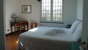 A bedroom with a bed, a desk, a chair, a window with curtains, and a framed picture on the wall.