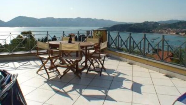 A terrace with a table and chairs overlooking a body of water and distant mountains.