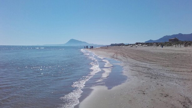 Een strand met een heldere lucht, een rustige zee en verre bergen.