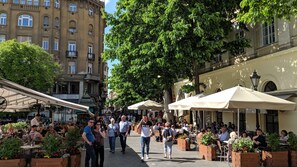 A bustling outdoor café area with tables and chairs, surrounded by buildings and trees. - Beside the Danube, UNESCO location with A/C. Quiet building in the City Centre (Budapest)