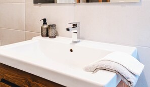 Un lavabo blanc pour la salle de bain, doté d’un robinet moderne, de deux distributeurs de savon et d’une serviette posée sur le côté.