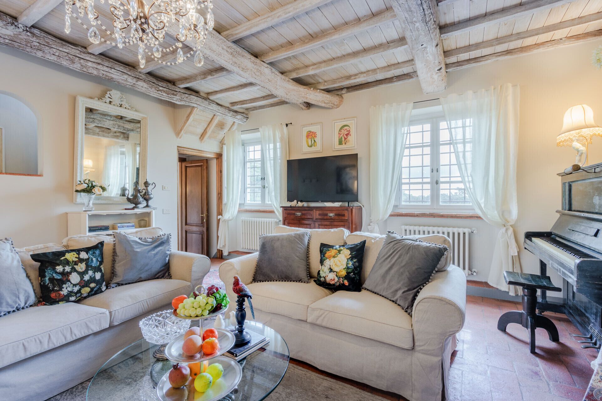 A living room with a sofa set, a glass coffee table with fruit, a piano, and a television.