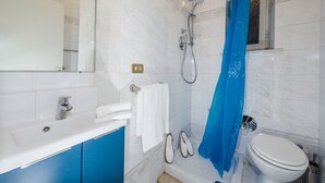 Une salle de bain avec un lavabo blanc, des meubles bleus, des toilettes blanches et une douche avec un rideau bleu.