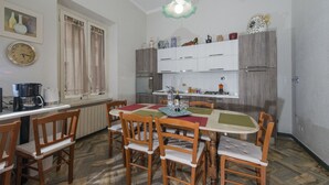 Un coin repas avec des chaises et une table en bois, des meubles de cuisine, une horloge et un luminaire suspendu.