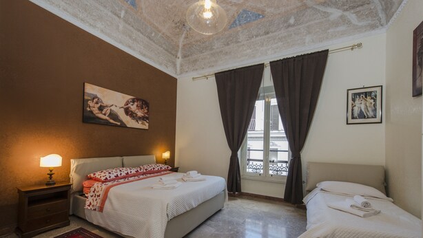 Une chambre d’hôtel avec deux lits, un tapis rouge, un tableau au mur et une fenêtre avec des rideaux.