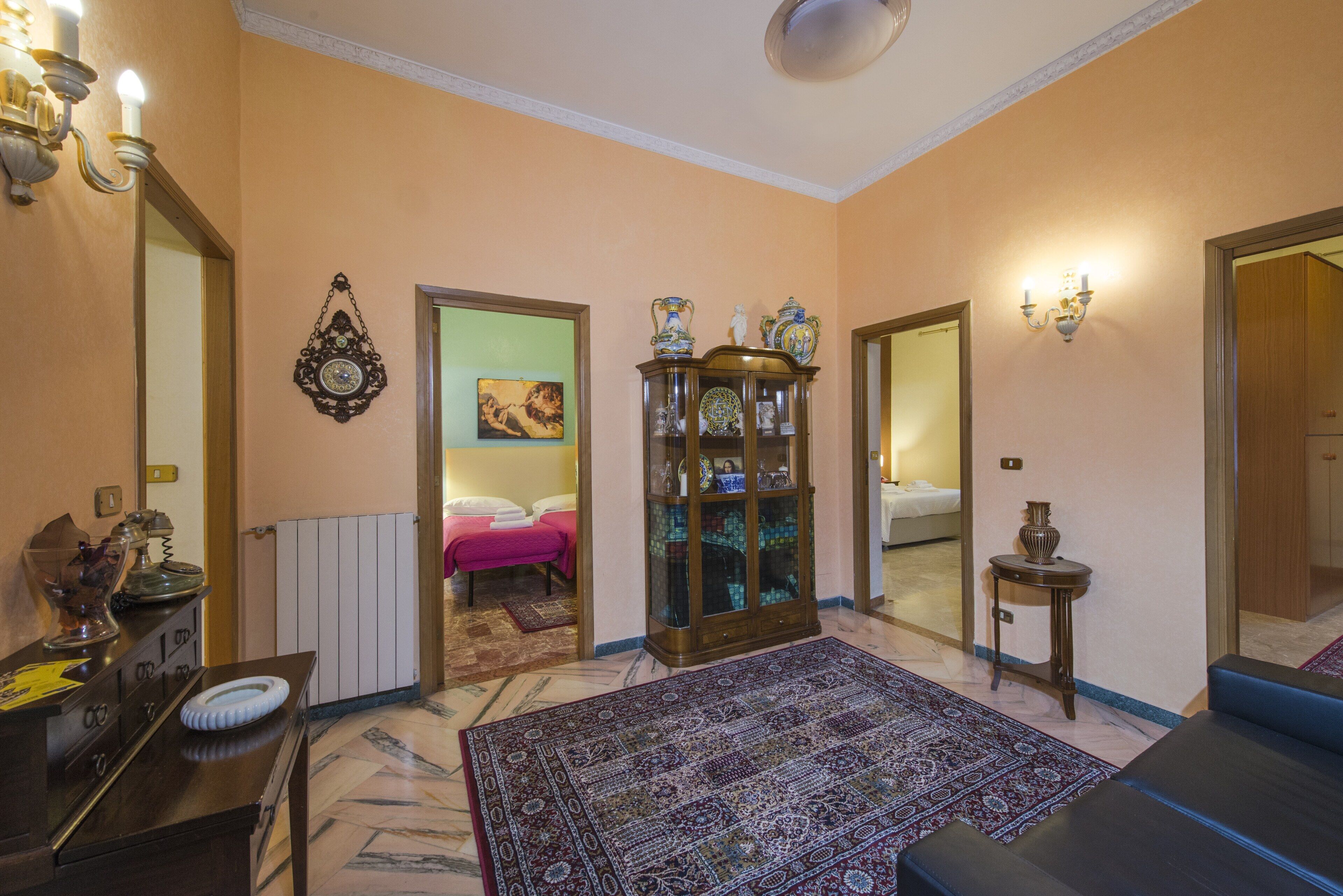 Une chambre d’hôtel avec un grand tapis à motifs, une armoire en bois ornée d’objets décoratifs, un miroir et un lit recouvert d’une couvre-lit rose.