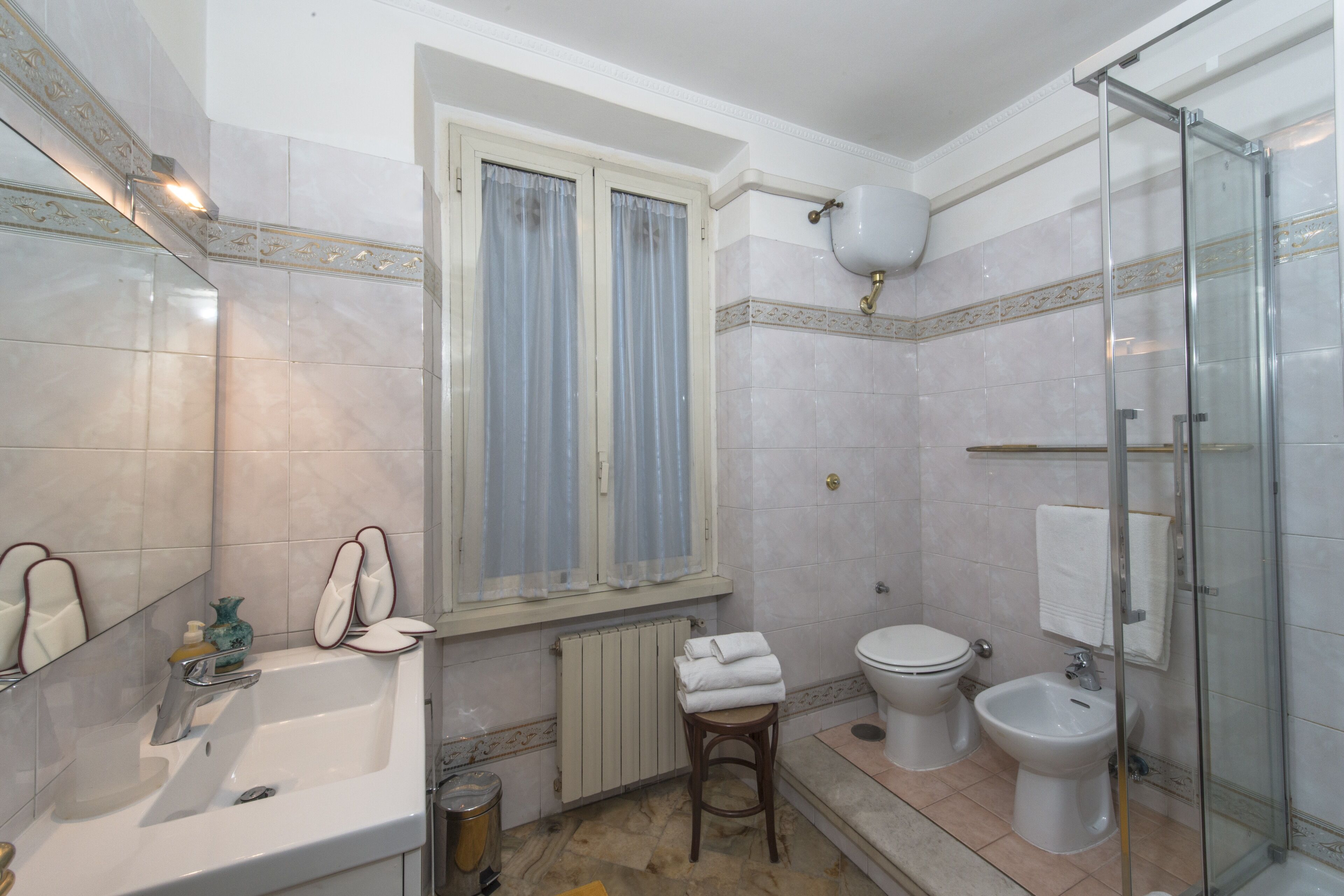 A bathroom with a sink, mirror, window, toilet, bidet, and shower.
