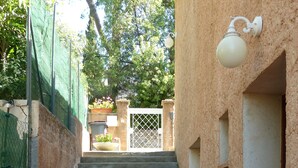 Un estrecho pasillo exterior con suelo de baldosas que conduce a una serie de escalones de hormigón. Hay plantas en macetas en la base de la escalera y un aplique en la pared a la derecha.