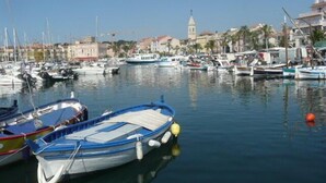 Un puerto deportivo con varias embarcaciones amarradas, una iglesia con una torre destacada al fondo y edificios a lo largo de la costa.